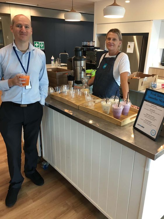 Sunwater corporate event — barista serving fresh juice at a white juice bar cart with colourful smoothies on display