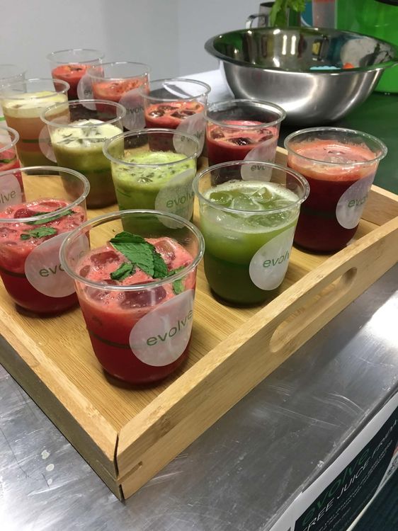 Fresh cold-pressed juices and smoothies on wooden serving tray at a corporate event — vibrant reds, greens, and purples