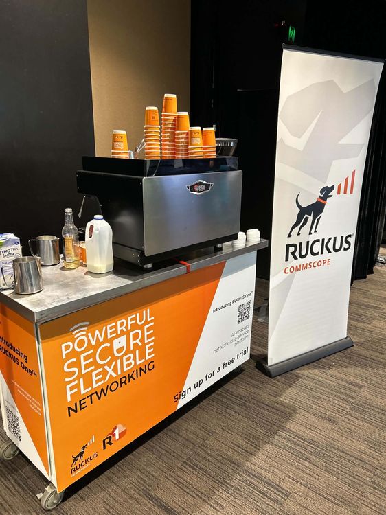 Ruckus CommScope branded mobile espresso cart at a Brisbane conference — orange branded cart with Wega machine